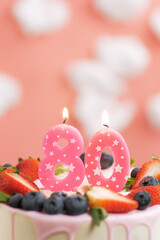 Birthday cake number 80. Beautiful pink candle in cake on pink background with white clouds. Close-up and vertical view