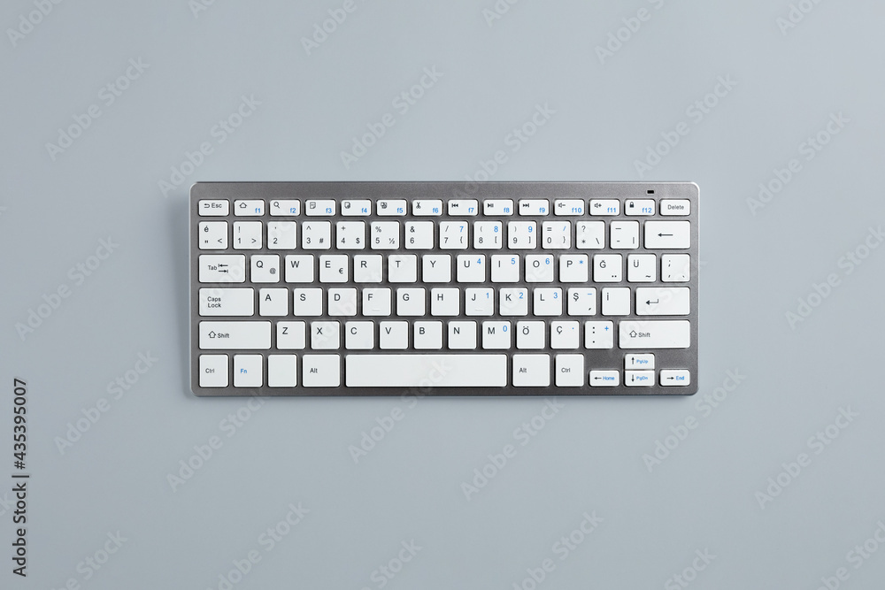 Poster computer keyboard with white buttons and metallic cover on gray background with copy space.