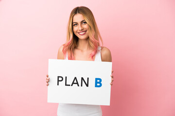 Young woman over isolated pink background holding a placard with the message PLAN B with happy expression