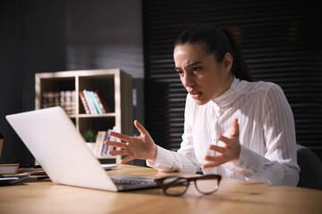 Emotional young businesswoman working on laptop in office. Online hate concept