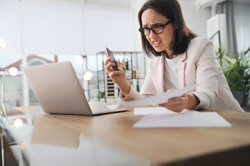 Emotional businesswoman with smartphone near laptop in office. Online hate concept