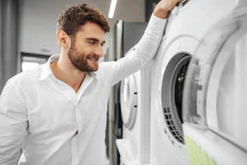 Young man choosing new washing machine in household appliances store
