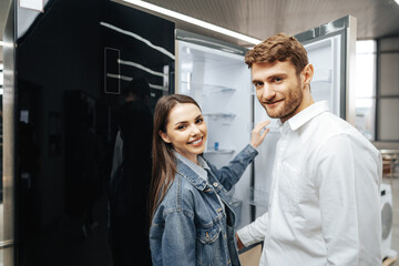Young couple selecting new refrigerator in household appliance store