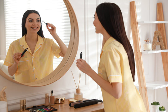 Young woman doing makeup near mirror at home. Morning routine