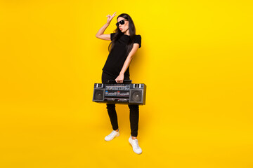 Fototapeta premium Full body photo of excited person hand hold boombox fingers show v-sign isolated on yellow color background
