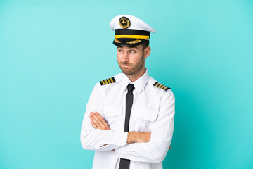 Airplane caucasian pilot isolated on blue background making doubts gesture while lifting the shoulders