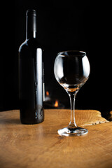 Wine, wine bottle and empty glass on rustic wooden surface with fire in the background, low key image, dark background, selective focus.