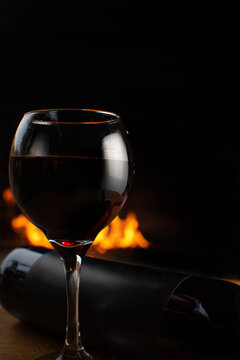 Wine, full wine glass and wine bottle lying on rustic wooden surface with fire in the background, low key image, dark background, selective focus.