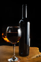 Wine, full wine glass and wine bottle on rustic wooden surface with fire in the background, low key image, dark background, selective focus.