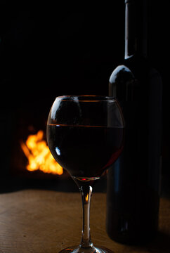 Wine, full wine glass and wine bottle on rustic wooden surface with fire in the background, low key image, dark background, selective focus.