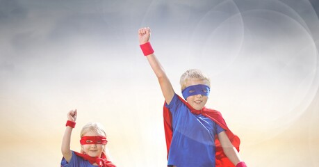 Composition of smiling caucasian boy and girl in superhero costumes with arms in air celebrating