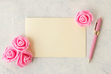 empty blank textured leaf with pink pen and pink roses on white concrete background. Congratulations or holiday concept.