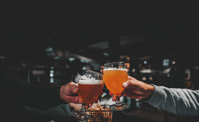 Closeup view of a two glass of beer in hand. Beer glasses clinking in bar or pub