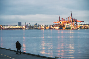 Young couple embracing on coastline and industrial cargo ship on harbor in Stanley Park