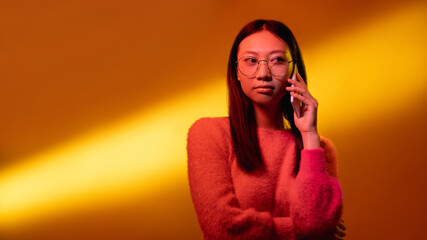 Business call. Neon light portrait. Mobile communication. Confident Asian woman in pink in glasses...