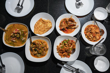 Variety of Thai food with spicy soup, fried fish, tofu, chicken curry, salad and silverware on dining table at dinner