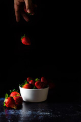 Frozen movement of a strawberry falling from the cook's hand into a bowl with more strawberries. Dark Food Photography