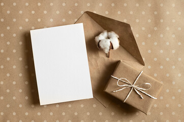 Greeting card mockup with gift box, envelope and cotton flower on craft paper background