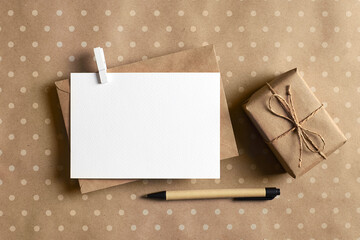 Greeting card stationary mockup with envelope, pen and gift box on craft paper background