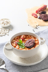 Asturiana traditional fabada with haricot, blood sausage on a white table. Vertical orientation. Spanish cuisine. Close up.