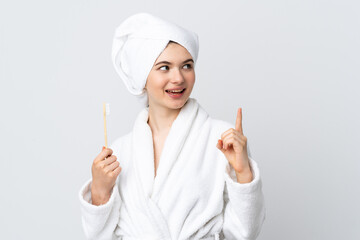 Young woman in a bathrobe holding toothbrush intending to realizes the solution while lifting a finger up
