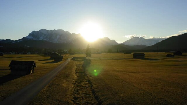 Drone shooting farmland with wooden houses located in valley in foot of snowy mountains, aerial bird's eye view of picturesque rural environment with homestead huts during sundawn