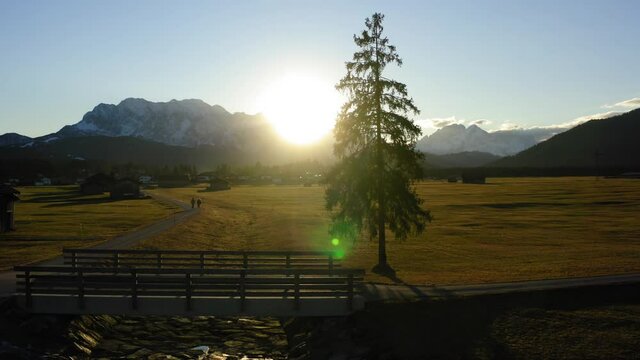 Drone shooting farmland with wooden houses located in valley in foot of snowy mountains, aerial bird's eye view of picturesque rural environment with homestead huts during sundawn