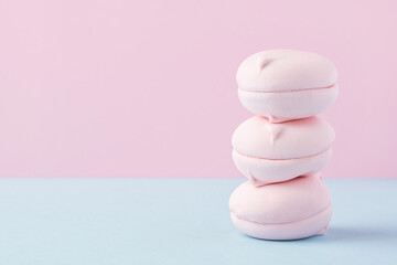 Fototapeta na wymiar Stack of pink marshmallows on combined pink and blue background. A pile of round shaped zephyr. Balance and minimalism concept in vegan sweets.