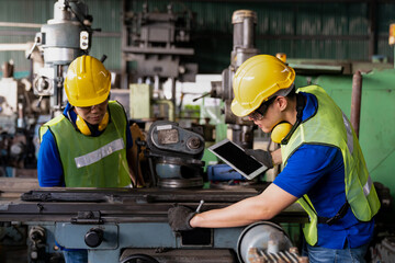 Two Asian engineer male worker maintaining machine lathe metal at the industry factory. Group of Asian Factory worker check or maintenance CNC machine in industry factory