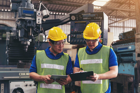 Asian factory male worker discussing and looking clipboard document for maintenance machine lathe metal in the industry factory. Engineer worker using manual document for lathe machine in the factory