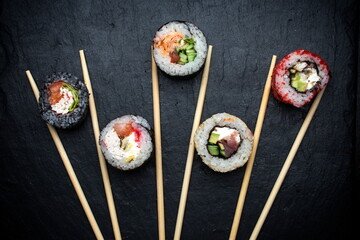 different sushi rolls on a black background with chopsticks