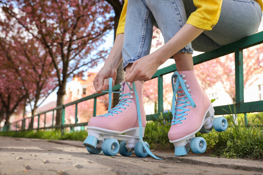 Young woman putting on roller skates outdoors, closeup
