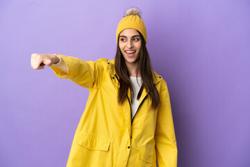 Young caucasian woman wearing a rainproof coat isolated on purple background giving a thumbs up gesture