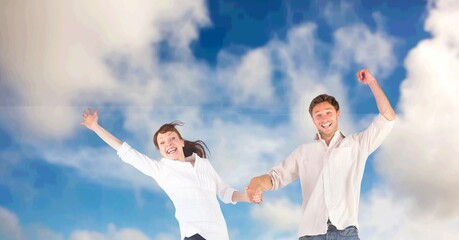Composition of happy couple celebrating, holding hands jumping in the air smiling, over blue sky