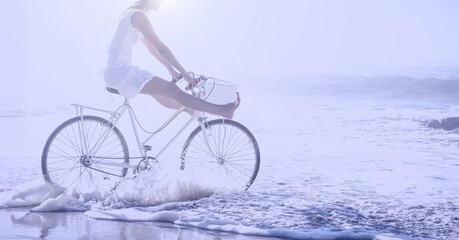 Fototapeta premium Composition of woman riding bike on beach with copy space