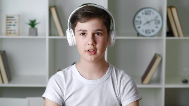 Portrait Of Handsome Boy Of 13 Years Old Puts On Headphones And Looks At The Camera, Against The Background Of A Home Interior.