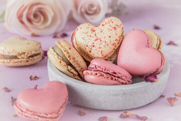 Heart shaped sweet macarons and roses in pastel colors on a pink base. A delicious dessert or gift for Valentine's Day or Mother's Day.