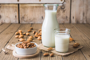 Glass and pitcher with vegan almond milk, almond kernels and whole almonds on an old rustic wooden...