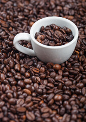 White espresso cup with fresh raw coffee beans inside beans background.