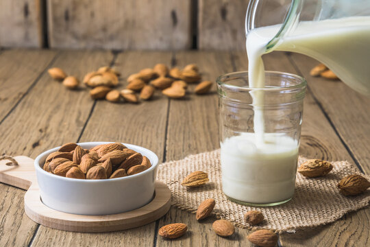 Vegan almond milk pouring into a glass, almond kernels and whole almonds on the old rustic wooden table