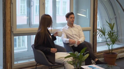 Formally dressed male and female administrators communicate during work break in office, Caucaisan colleagues with coffee cups discussing exchange experience and business plans