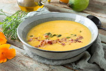 a plate of pumpkin soup with bacon and parsley on a wooden table close-up