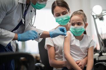 An experienced pediatrician vaccinates a little girl, the mother holds the baby in her arms, the...