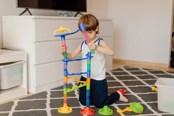 3 year old boy is building plastic construction sitting on floor of house. Concept of loneliness...
