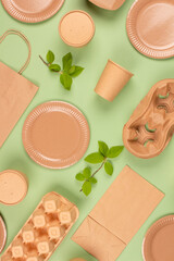 Flat lay composition with eco-friendly tableware and kraft paper food packaging on green background. Sustainable packaging, recyclable paperware, zero waste packaging concept. Mockup, vertical image
