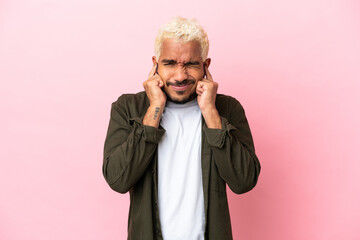 Young Colombian handsome man isolated on pink background frustrated and covering ears