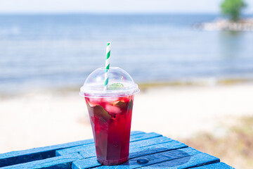 ice drink red lemonade soda on the beach cherry or strawberry fresh juice, sea coast shore, summer surf wave background refreshing relax positive mood vacation top view