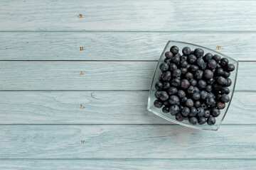 Blueberries in a glass bowl on wooden table top. Top view with copy space. Flat lay.