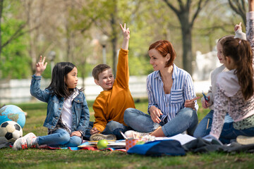 Teacher with small children sitting outdoors in city park, learning group education concept.
