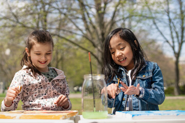 Small children painting pictures outdoors in city park, learning group education concept.